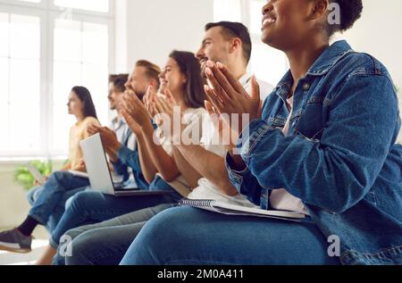 Zufriedene, vielfältige Zielgruppe von Studenten oder Arbeitern, die während eines Vortrags oder Seminars applaudieren. Stockfoto