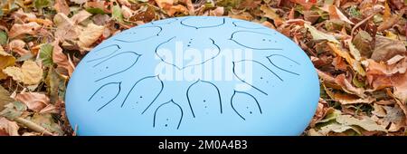 Blaue Zungentrommel aus Stahl auf einem Boden, der mit trockenen Blättern bedeckt ist, Schlaggerät, das häufig für Meditation und Tontherapie verwendet wird Stockfoto