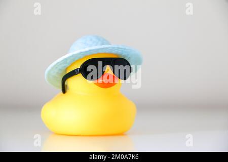 Sommerente aus gelbem Gummi mit schwarzer Sonnenbrille und hellblauem Hut. Sommer- und Hitzewetterkonzept. Stockfoto