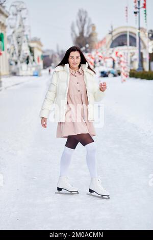 Brünette Frau läuft draußen Schlittschuh. Neujahrsferien, gute Laune. Träume werden wahr Konzept. Stockfoto