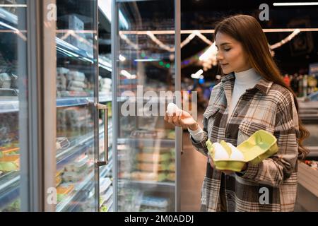 Junge Frau wählt sorgfältig Eier in einem Lebensmittelgeschäft aus Stockfoto