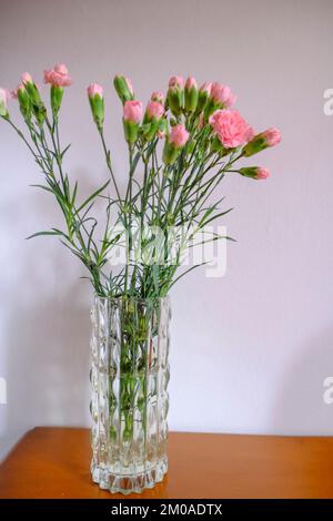 Strauß rosa Nelken in einer Kristallvase an der weißen Wand in der Holzschublade. Speicherplatz kopieren. Inneneinrichtung Stockfoto