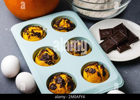 Kürbis-Muffins, gebacken in der Silikonform am Tisch mit Zutaten. Muffin-Bäckerei mit hausgemachtem Kochhintergrund Stockfoto