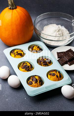 Kürbis-Muffins, gebacken in der Silikonform am Tisch mit Zutaten. Muffin-Bäckerei mit hausgemachtem Kochhintergrund Stockfoto