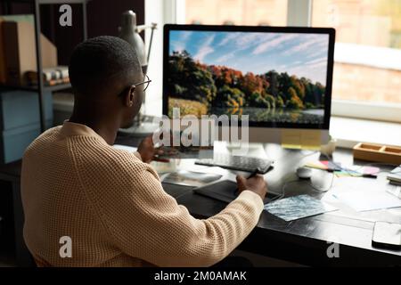 Professioneller Fotograf, der Fotos am Computer am Schreibtisch in seinem Heimbüro bearbeitet Stockfoto