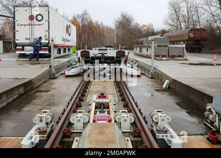 05. Dezember 2022, Sachsen, Leipzig: Ein Mann sieht zu, wie ein Sattelschlepper auf einem Güterbahnhof mit einer neuen Ladetechnik auf einen Eisenbahnwaggon verladen wird. Das Leipziger Unternehmen CargoBeamer möchte den Güterverkehr innerhalb Europas effizienter und umweltfreundlicher gestalten. Im neu entwickelten Terminal können Lkw-Anhänger mit Hilfe einer sogenannten Laderampe seitlich auf den Waggon gefahren werden. Dadurch wird das Problem umgangen, dass fast alle Lkw-Anhänger nicht mit einem Kran angehoben werden können, was die Beladung der Schiene kostspielig und nicht lohnenswert macht. Das erste Terminal des Unternehmens ist in Calais in Nor in Betrieb Stockfoto
