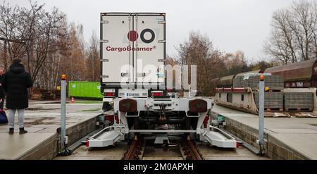 05. Dezember 2022, Sachsen, Leipzig: Ein Mann sieht zu, wie ein Sattelschlepper auf einem Güterbahnhof mit einer neuen Ladetechnik auf einen Eisenbahnwaggon verladen wird. Das Leipziger Unternehmen CargoBeamer möchte den Güterverkehr innerhalb Europas effizienter und umweltfreundlicher gestalten. Im neu entwickelten Terminal können Lkw-Anhänger mit Hilfe einer sogenannten Laderampe seitlich auf den Waggon gefahren werden. Dadurch wird das Problem umgangen, dass fast alle Lkw-Anhänger nicht mit einem Kran angehoben werden können, was die Beladung der Schiene kostspielig und nicht lohnenswert macht. Das erste Terminal des Unternehmens ist in Calais in Nor in Betrieb Stockfoto