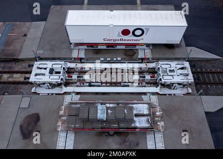 05. Dezember 2022, Sachsen, Leipzig: Ein Auflieger wird an einem Güterbahnhof mit einer neuen Ladetechnik auf einen Eisenbahnwagen verladen. Das Leipziger Unternehmen CargoBeamer möchte den Güterverkehr innerhalb Europas effizienter und umweltfreundlicher gestalten. Im neu entwickelten Terminal können Lkw-Anhänger mit Hilfe einer sogenannten Laderampe seitlich auf den Waggon gefahren werden. Dadurch wird das Problem umgangen, dass fast alle Lkw-Anhänger nicht mit einem Kran angehoben werden können, was die Beladung der Schiene kostspielig und nicht lohnenswert macht. Das erste Terminal des Unternehmens ist in Calais in Nordfrankreich in Betrieb Stockfoto