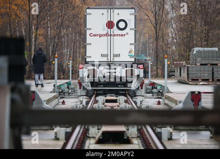 05. Dezember 2022, Sachsen, Leipzig: Ein Mann sieht zu, wie ein Sattelschlepper auf einem Güterbahnhof mit einer neuen Ladetechnik auf einen Eisenbahnwaggon verladen wird. Das Leipziger Unternehmen CargoBeamer möchte den Güterverkehr innerhalb Europas effizienter und umweltfreundlicher gestalten. Im neu entwickelten Terminal können Lkw-Anhänger mit Hilfe einer sogenannten Laderampe seitlich auf den Waggon gefahren werden. Dadurch wird das Problem umgangen, dass fast alle Lkw-Anhänger nicht mit einem Kran angehoben werden können, was die Beladung der Schiene kostspielig und nicht lohnenswert macht. Das erste Terminal des Unternehmens ist in Calais in Nor in Betrieb Stockfoto