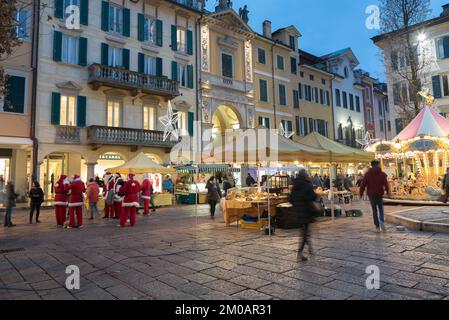 Stadtstraße in der Abenddämmerung mit Weihnachtslichtern und Verkaufsständen. Historisches Zentrum von Varese, Corso Matteotti Stockfoto