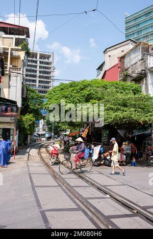 Hanoi, Vietnam - 16. September 2018: Hübsche vietnamesische Frau mit traditionellem Kopfschmuck überquert die Bahnstrecke auf einem Fahrrad Stockfoto