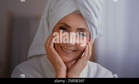 Sorgenfreies Porträt glückliche Seniorin mit Anti-Falten-Haut-Hydrogel-Kollagen-Pflastern unter den Augen, die lächelnd die alte 60s Weiße Frau mit Handtuch fotografieren Stockfoto