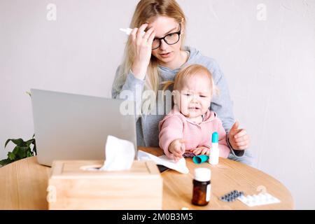 Porträt einer jungen Mutter, die am Tisch neben Laptop-Pillen sitzt, Blasen, mit einem kleinen Mädchen, das Rezept liest. Stockfoto