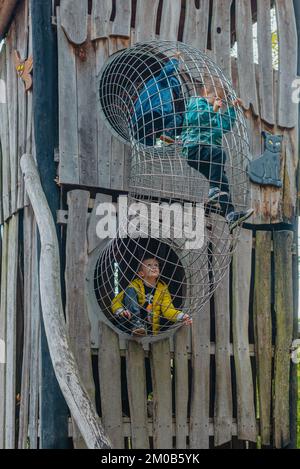 Ein Kind klettert an einem heißen Sommertag in einem Park auf einem Spielplatz auf ein Berggitter. Kinderspielplatz in einem öffentlichen Park, Unterhaltung und Erholung Stockfoto