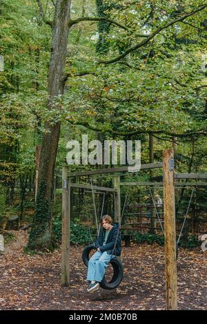 Ein Teenager, das auf einer Schaukel im Park sitzt. Nachdenkliches, trauriges Kind. Das Gedankliche Traurige Teenager-Mädchen Sitzt Am Kreisverkehr Auf Dem Spielplatz. Teenager-Mädchen traurig Stockfoto