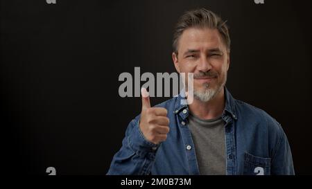 Ein Mann, der lächelt und Daumen nach oben zeigt. Porträt eines erwachsenen Mannes im Alter von 50s Jahren, glückliches selbstbewusstes Lächeln. Speicherplatz kopieren. Stockfoto