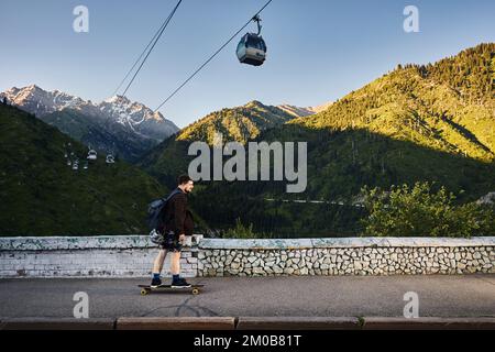 Bärtige Skater fahren auf der Bergstraße auf seinem Longboard in Medeo Dum Almaty, Kasachstan Stockfoto