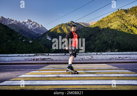 Bärtige Skater fahren auf der Bergstraße auf seinem Longboard in Medeo Dum Almaty, Kasachstan Stockfoto