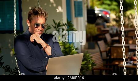 Außenporträt eines erwachsenen Mannes in 50s, glückliches selbstbewusstes Lächeln. Arbeiten mit einem Laptop im Heimbüro. Reif, mittelalt, bärtig. Stockfoto