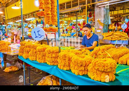 BANGKOK, THAILAND - 23. APRIL 2019: Der Verkäufer stellt rituelle Ringelgirlanden in einem kleinen Stall des Blumenmarktes von Pak Khlong Talat her, am 23. April in Bangkok Stockfoto