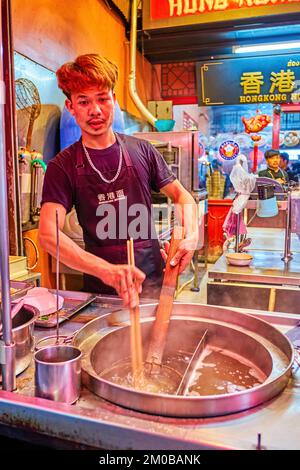 BANGKOK, THAILAND - 23. APRIL 2019: Der junge Koch bereitet traditionelle Speisen in der Küche des chinesischen Restaurants im Sampeng Lane Markt von C zu Stockfoto