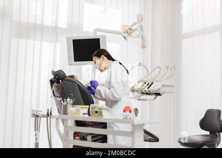 Schönes Lächeln mit weißen Zähnen. Asiatischer Zahnarzt behandelt Zähne eines jungen schönen Mädchens mit einem Zahnbohrer durch eine Lupe in der Zahnarztpraxis. Stockfoto