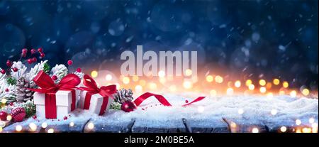 Geschenkbox Auf Schnee Im Winterblauen Hintergrund – Weihnachtsgeschenke Und Rote Dekoration In Verschneiter Nacht Mit Abstrakten Unschärfe-Bokeh-Lichtern Stockfoto