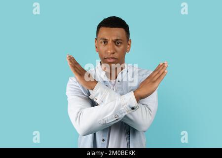 Trauriger, seriöser, gutaussehender, junger afroamerikanischer Mann, der zwanglos die Arme gekreuzt hat und ein Stoppschild macht Stockfoto