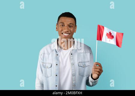 Glücklicher junger afroamerikanischer Student in zwangloser Show Canada Flag, isoliert auf blauem Hintergrund, Studio Stockfoto