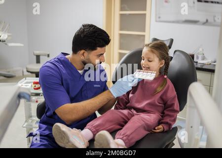 Zahnzähntonpalette. Stomatologe Kieferorthopäde männlicher Zahnarzt wählt die Farbe der süßen Zähne des kleinen Vorschulmädchens für die Aufhellung in der Klinik aus. Stockfoto