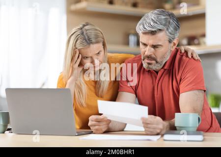 Ängstlicher Mann und Frau mittleren Alters, die Korrespondenz überprüfen, Kücheneinrichtung Stockfoto