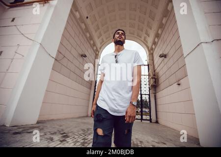 Ein afroamerikanischer Mann in einem weißen, leeren T-Shirt geht die Straße entlang. Modell. Stockfoto