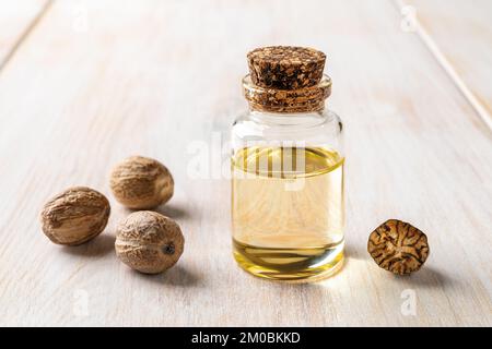 Glasbecher mit ätherischem Muskatöl. Muskatnuss-Duftöl und Samen in einer kleinen Flasche auf weißem Holzhintergrund. Myristica duftet Baumfrucht Stockfoto