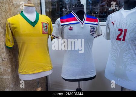 Selten,authentisch,Fußball,Trikots,nicht,Fan,Replica,Fußballtrikots,ein,Display,während,Katar,Weltmeisterschaft,Winter,2022,in,Shop,Schaufenster,Schaufenster,at,Clive,kontinentale Herrenbekleidung,Shop,Terrace Road,Aberystwyth,Stadt,Zentrum,West,Wales,GB,Großbritannien,Großbritannien. Das Display,geliehen,von,Fußball,Sammler,umfasst,zwei England Trikots,A,gelbes walisisches Trikot,und,A,Senegal,Trikot,und,Fußball,Schuhe,getragen,und,signiert,von,Walisisch,Fußball,Legende,Gareth Bale. Das gelbe Hemd ist ein passend getragenes Wales-Hemd, getragen, AT, Weltmeisterschaft 1958. Klassisch, 1981 England, Hemd, Nummer 7, getragen, von Kevin Keegan. Stockfoto