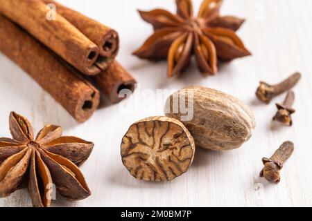 Ganze und halbierte Muskatnusssamen, Zimtstangen, wenige Nelken und Sternanis auf weißem Holzhintergrund. Kürbisgewürzezutaten. Stockfoto