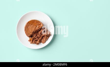 Weiche Pastete für Katze auf einem Futterteller auf pastellfarbenem Minzgrün-Hintergrund. Anteil von nassem Heimtierfutter aus Hackfleisch auf einer weißen Untertasse. Nasses Haustierfutter. Stockfoto