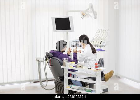 Medizin, Zahnheilkunde und Zahnpflegekonzept. Weibliche junge asiatische Zahnärztin zeigt Röntgenbild einem attraktiven Patienten, bärtigen Mann in einer modernen leichten Zahnklinik. Stockfoto