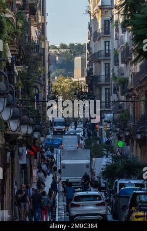 Enge Straße in Barcelona, voll mit Menschen, die auf dem Bürgersteig mit Fahrrädern laufen und viel Verkehr bei Sonnenaufgang Stockfoto