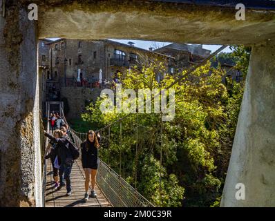 Die Leute überqueren die Hängebrücke von Rupit und alte Häuser im Hintergrund Stockfoto