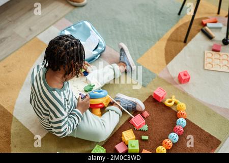 Großer Blickwinkel auf den süßen schwarzen Jungen, der mit bunten Spielzeugen auf dem Boden spielt, Fokus auf geflochtenes natürliches Haar, Kopierbereich Stockfoto