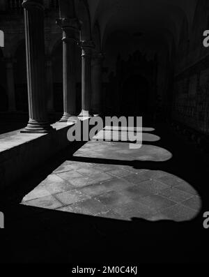 Kunstvoll verzierte mittelalterliche Bögen, die ihren eigenen Schatten und ihre eigene Silhouette erzeugen. Hinter dem Kloster und den blauen Fliesen, die die Wände der Kloiste bedecken Stockfoto