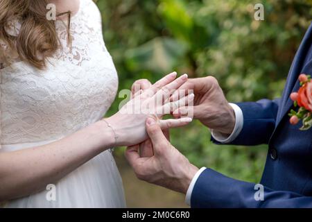 Ein Bräutigam legt der Braut einen Ehering an den Finger Stockfoto