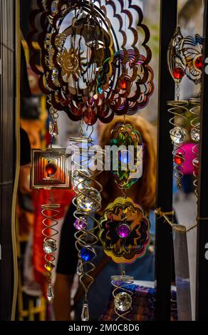 Verschiedene Objekte mit farbigen Steinen und großen Anhängern mit goldenen geometrischen Formen in einem Geschenkstand und eine Frau im Hintergrund mit ihrer Face Cove Stockfoto