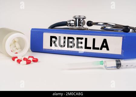 Medizinisches Konzept. Auf einer weißen Oberfläche befinden sich Pillen, eine Spritze, ein Stethoskop und eine Mappe mit der Aufschrift - Rubella Stockfoto