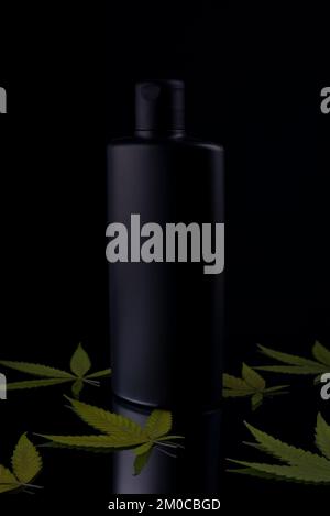 Hanfshampoo. Schwarze Shampooflasche mit Cannabis auf schwarzem Hintergrund Stockfoto