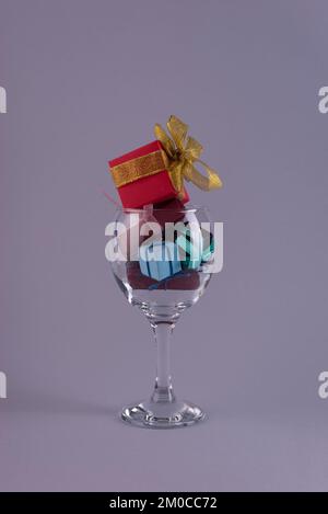 kleine weihnachtsgeschenke in einem Weinglas auf grauem Hintergrund Stockfoto