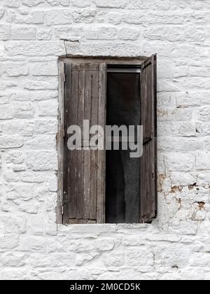 APULIEN, ITALIEN - 18. OKTOBER 2022: Altes braunes Holzfenster mit Rollläden in weißer Steinwand Stockfoto