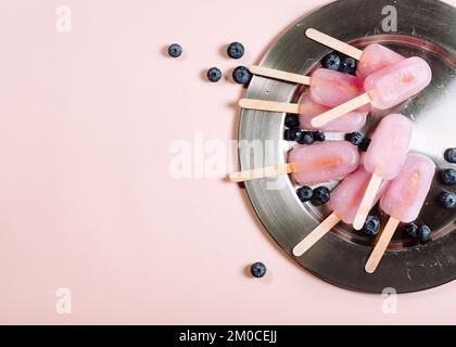 Rosa Eis am Stiel mit Blaubeeren auf einem Tablett, Draufsicht. Stockfoto