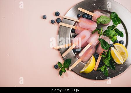 Rosa Eis am Stiel auf einem Tablett mit Blaubeeren, Zitrone und Minze. Stockfoto