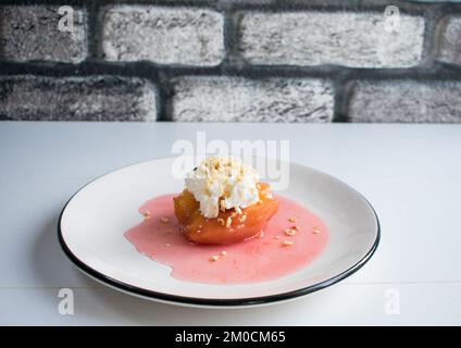 Traditionelles türkisches Quittendessert, Quitten wird in Wasser mit Zucker gekocht und mit Sahne und Haselnuss serviert. Stockfoto